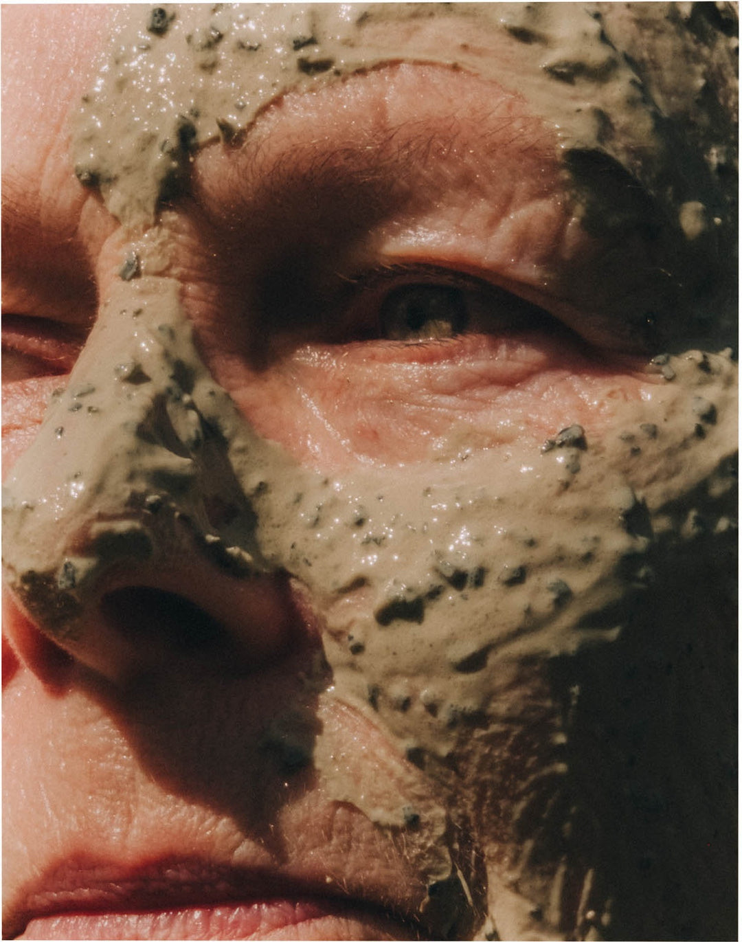 A close-up of a face wearing a seaweed treatment mask in bright sunlight