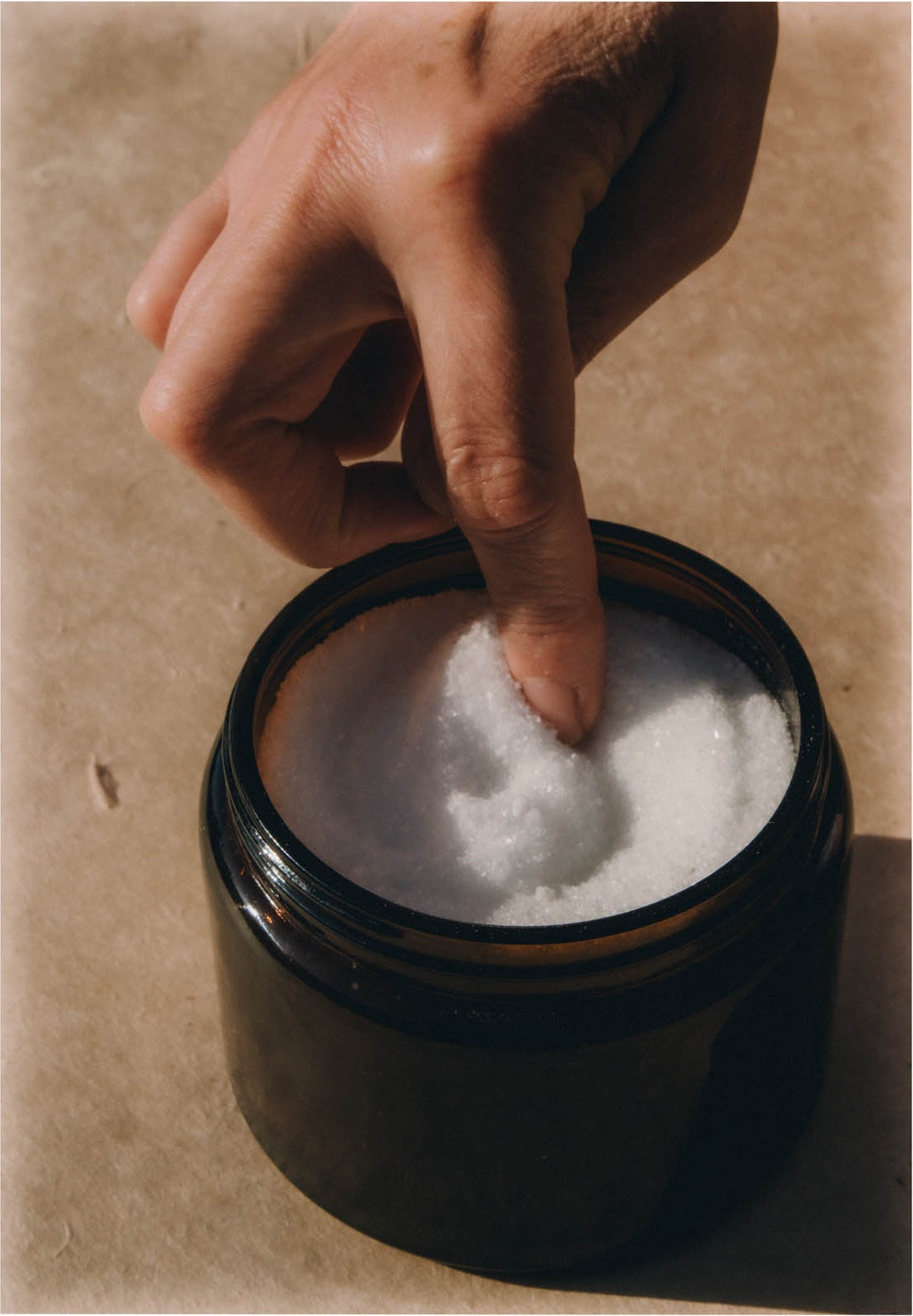 A finger lifting sea salt from an amber jar