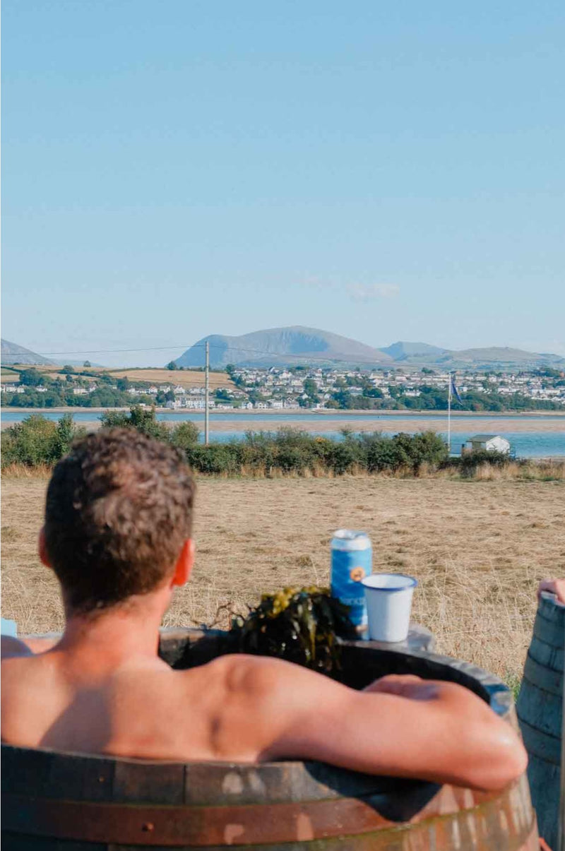 A bather in a barrel seaweed bath looking across the water to the mountains