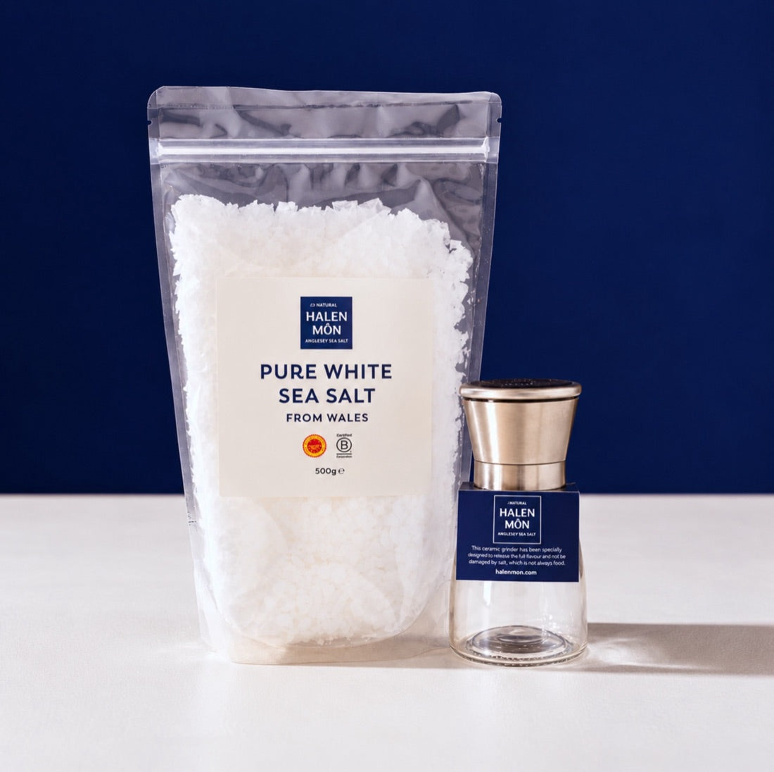 A 500g bag of Halen Môn Pure White Sea Salt next to a stainless steel Halen Môn mill